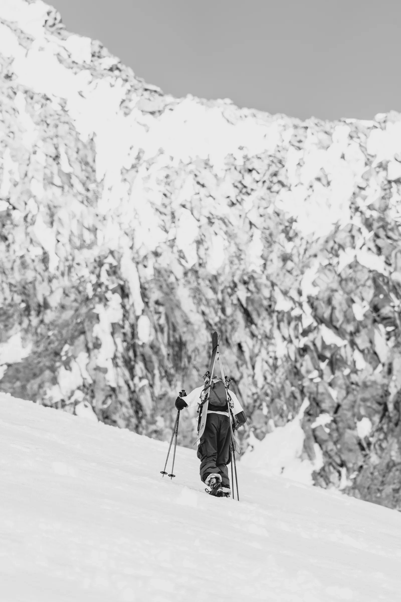 A skier carrying equipment up a steep snow slope