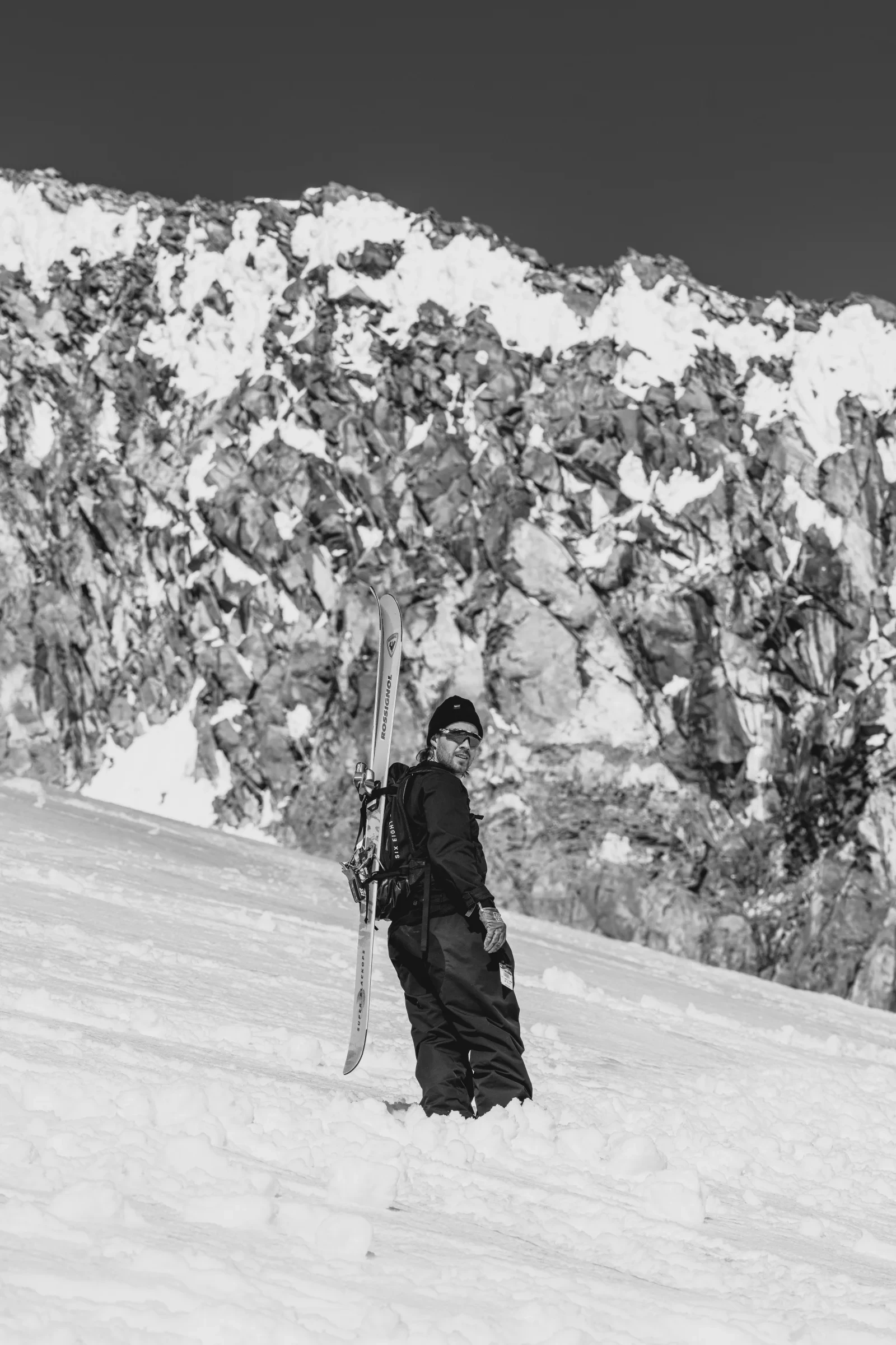 A skier pausing below a broken alpine ridge