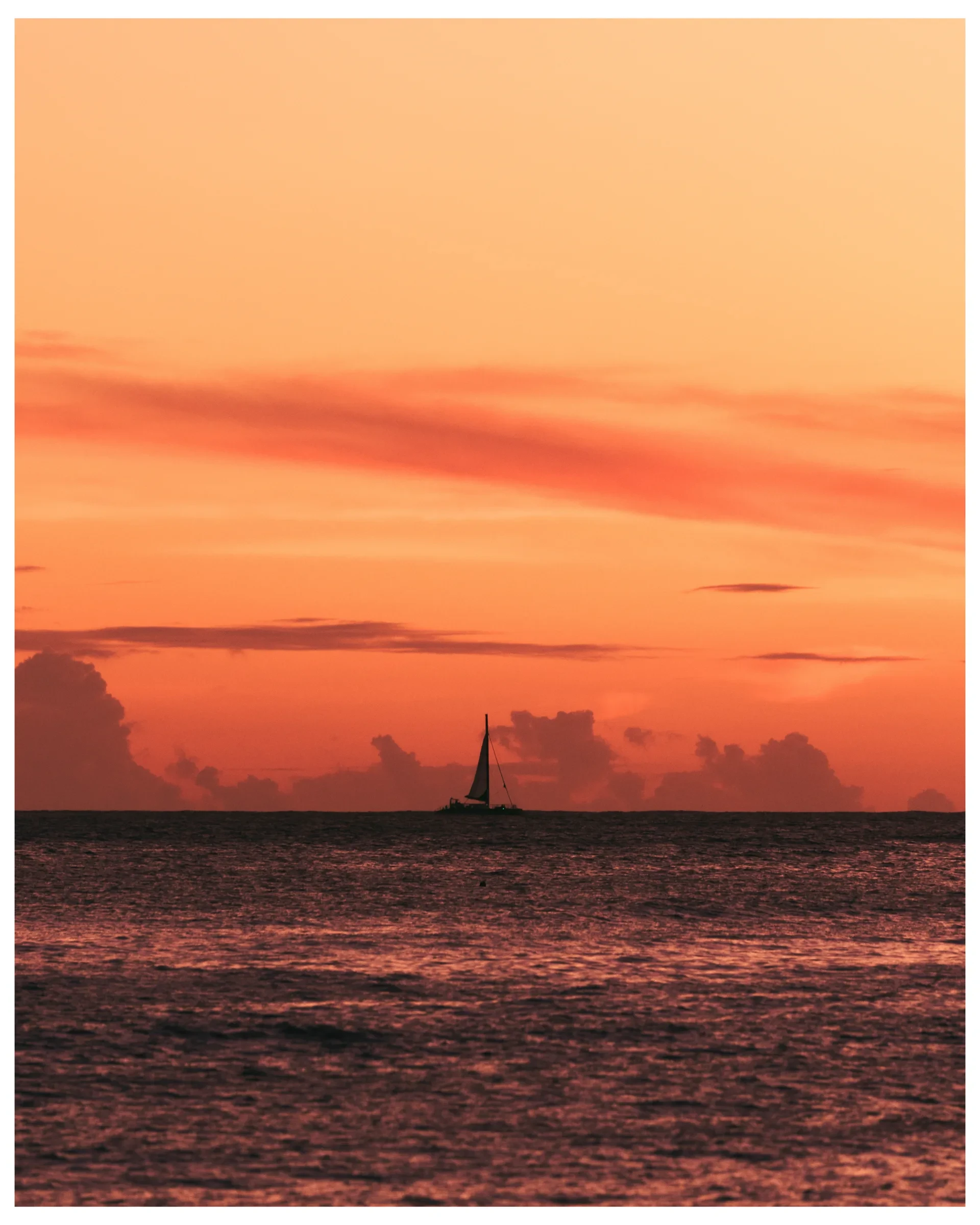 A sailboat crossing calm water at sunset