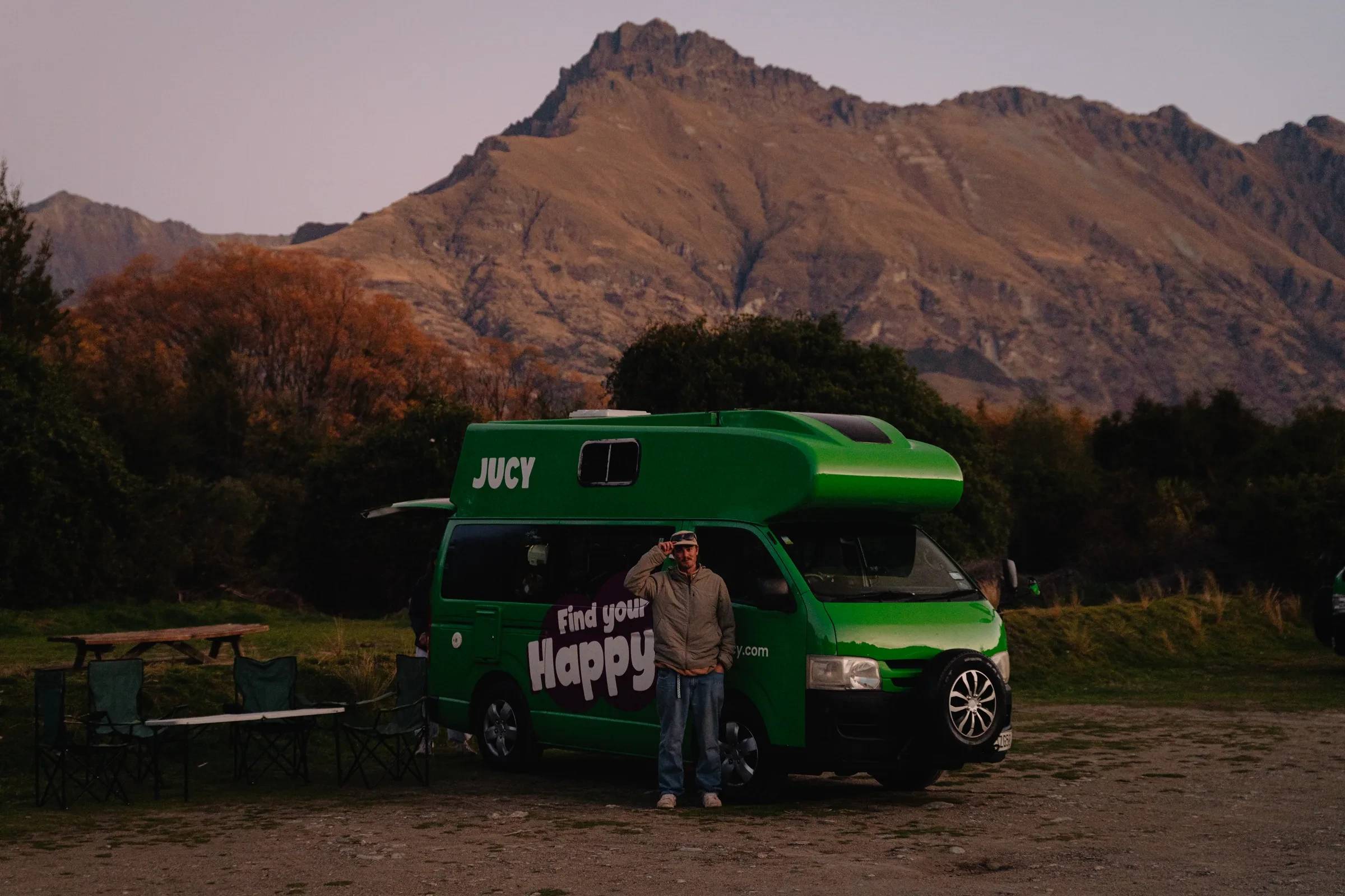 A green camper van beneath a mountain range